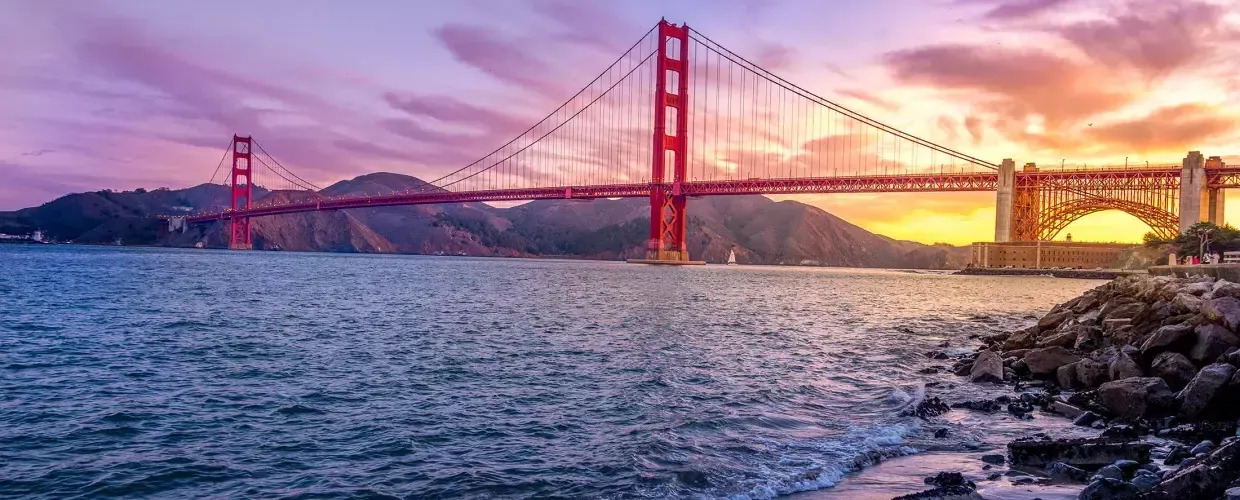 A Ponte Golden Gate ao pôr do sol 和 um céu multicolorido e a Baía de 贝博体彩app em primeiro plano.